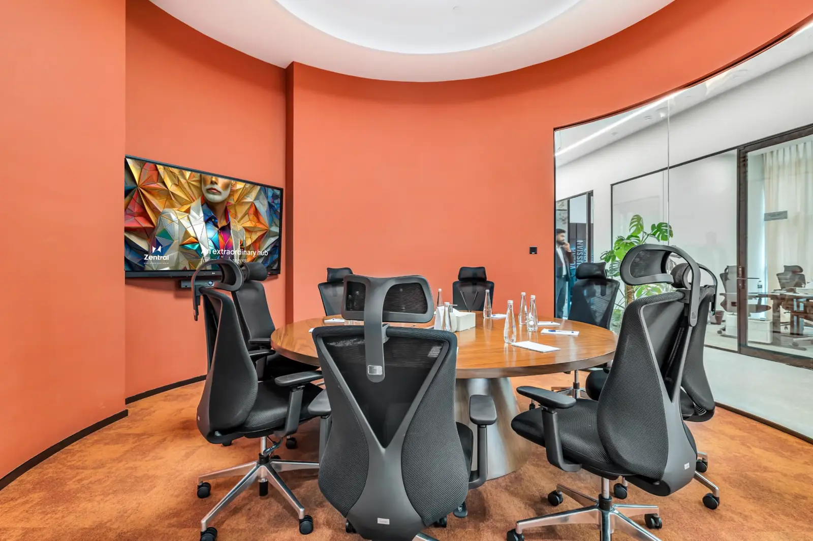 A Zentral meeting room with a round wooden table, ergonomic chairs and a wall screen