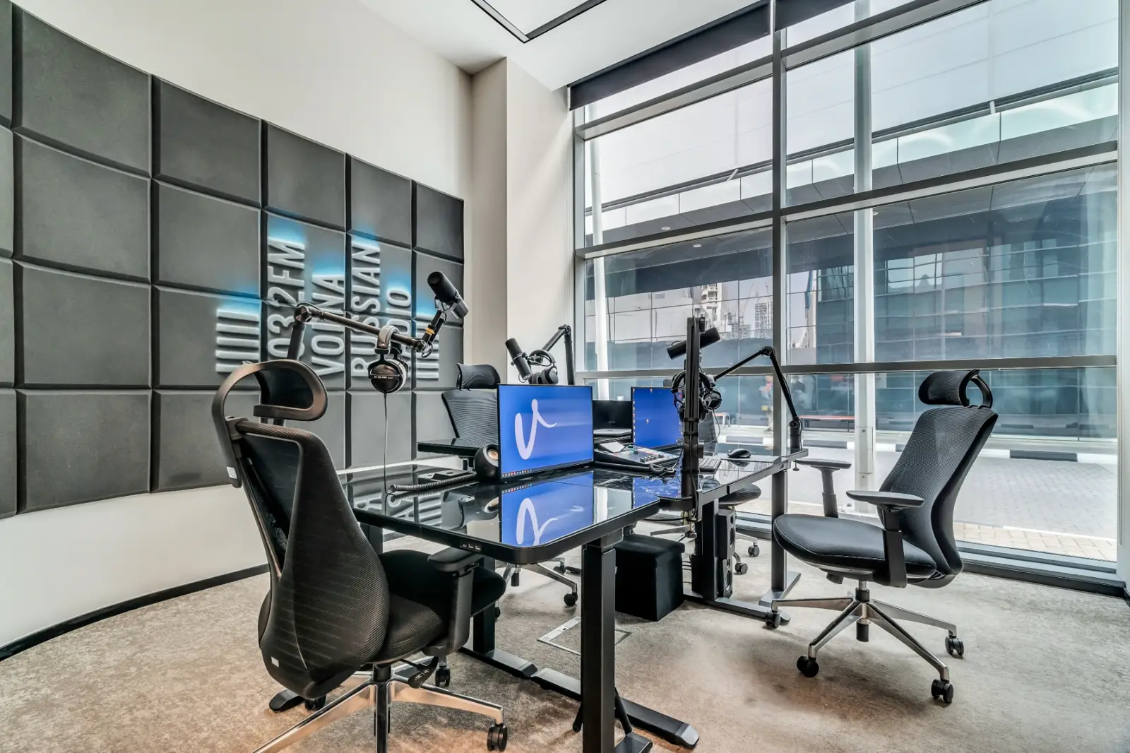A member's private office with desks, monitors and microphone equipment by large windows