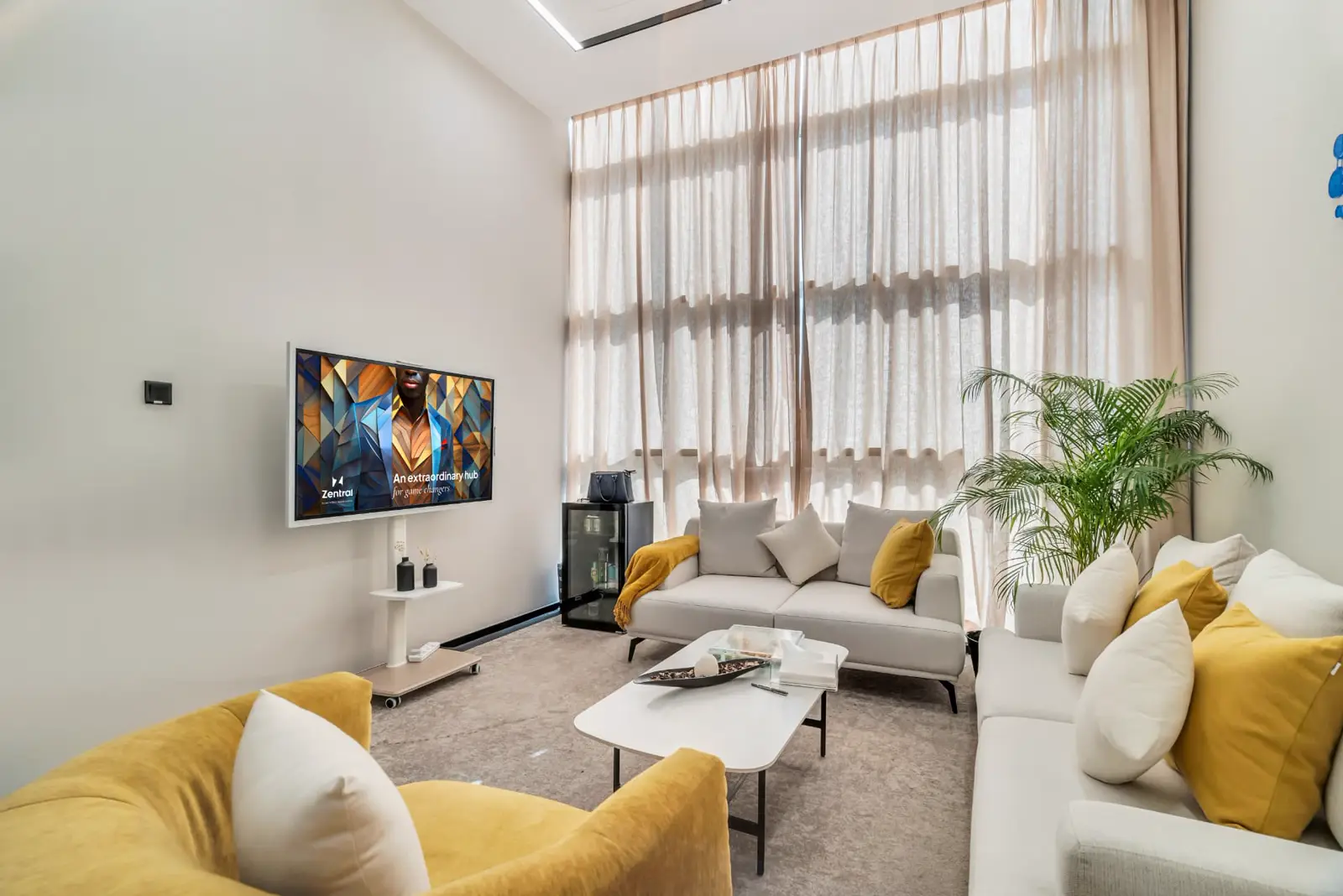 A Zentral business lounge with sofas, a TV screen and tall curtained windows
