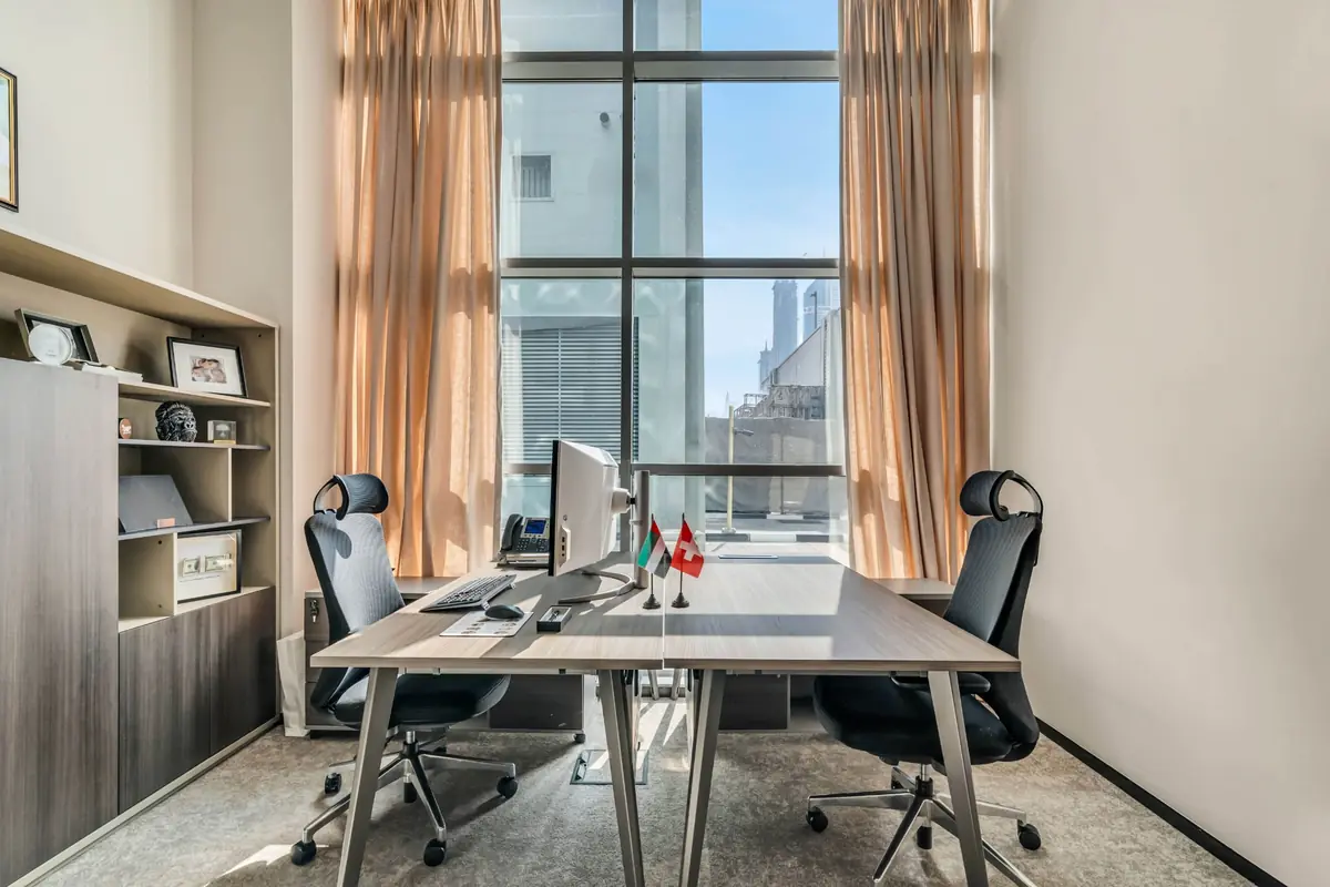 A furnished private office with two desks and tall windows